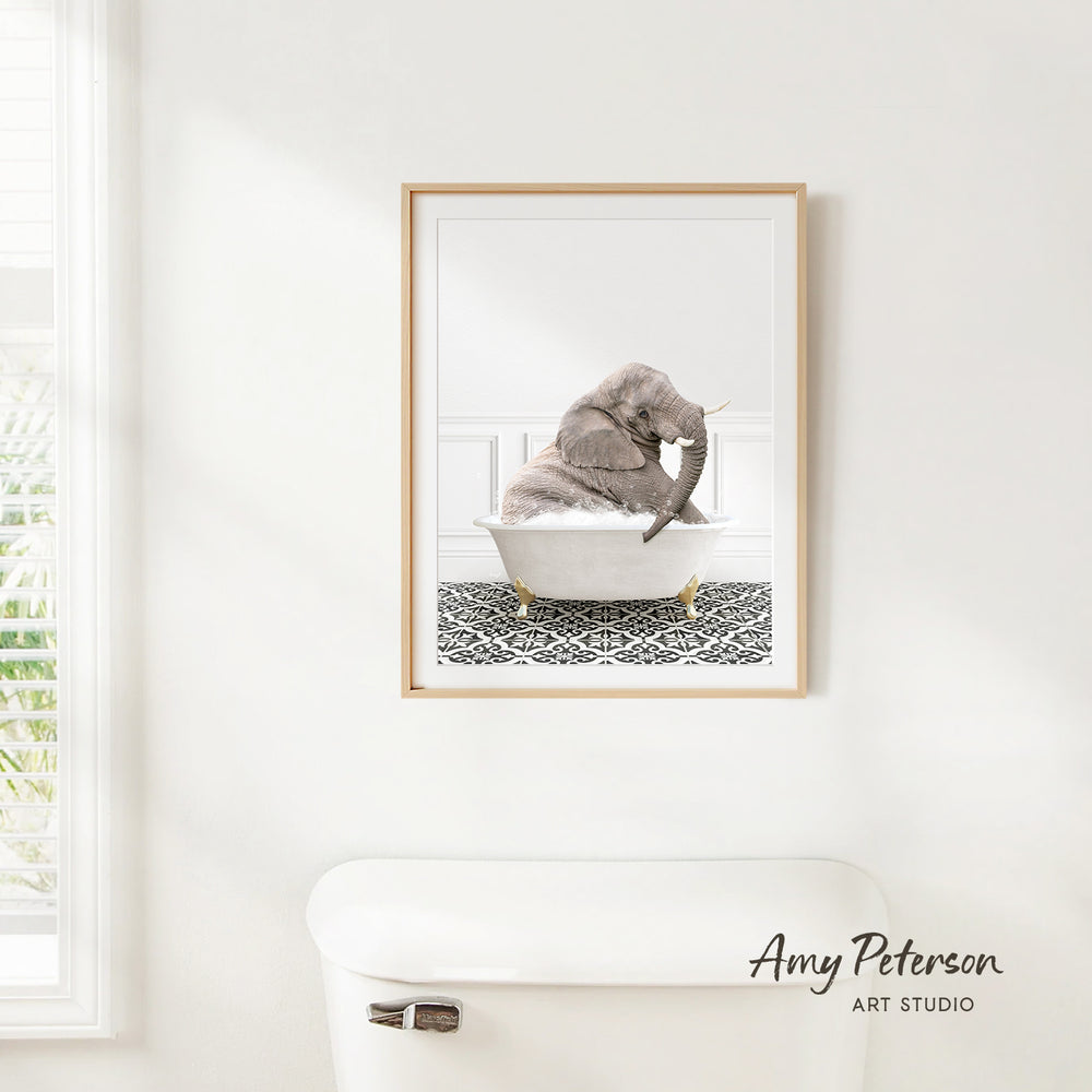 A framed image of an elephant sitting in a bathtub is hanging on a white wall.