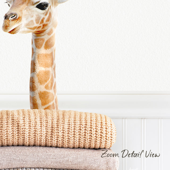 A giraffe's head is visible peeking over a stack of beige blankets, with a white wall in the background.
