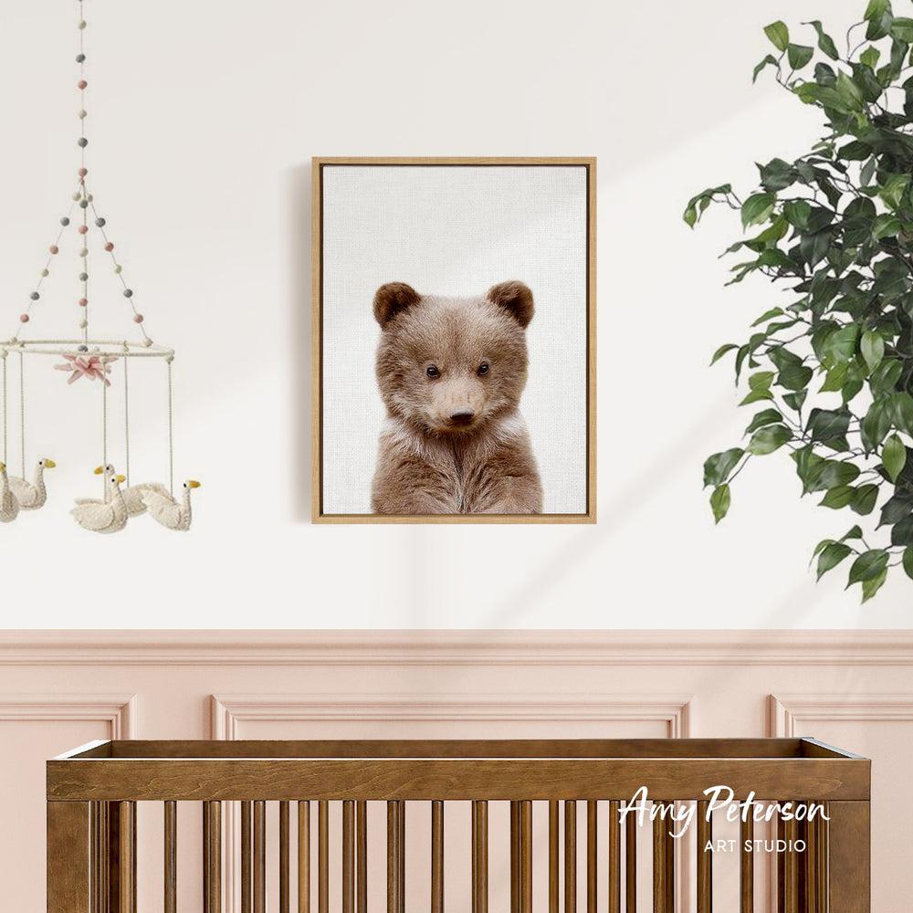 a wooden crib with a framed picture of a brown bear hanging on the wall above it.