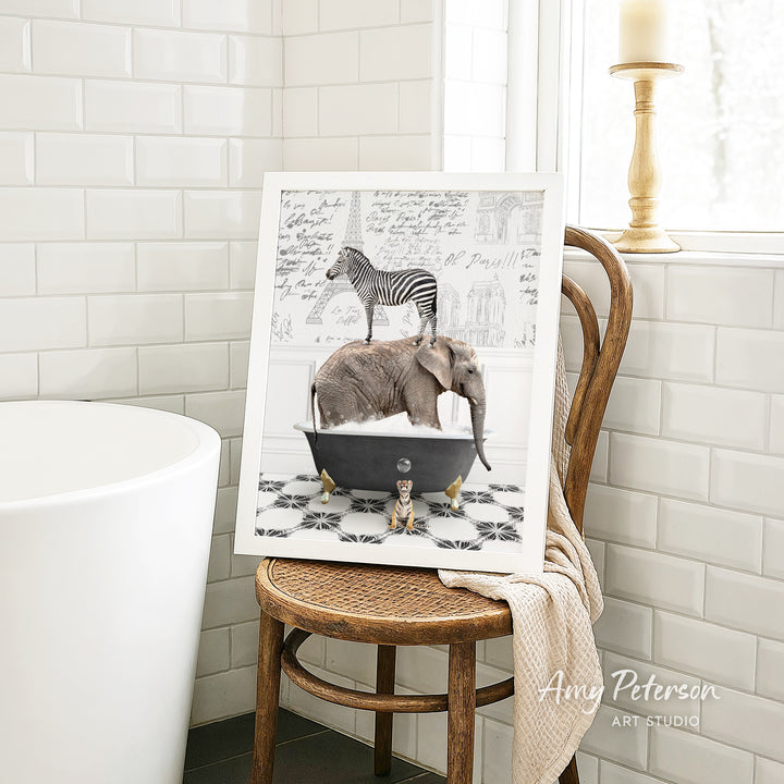 A framed image depicting a zebra standing on an elephant in a bathtub, with a towel draped over the back of a wooden chair in a bathroom setting.