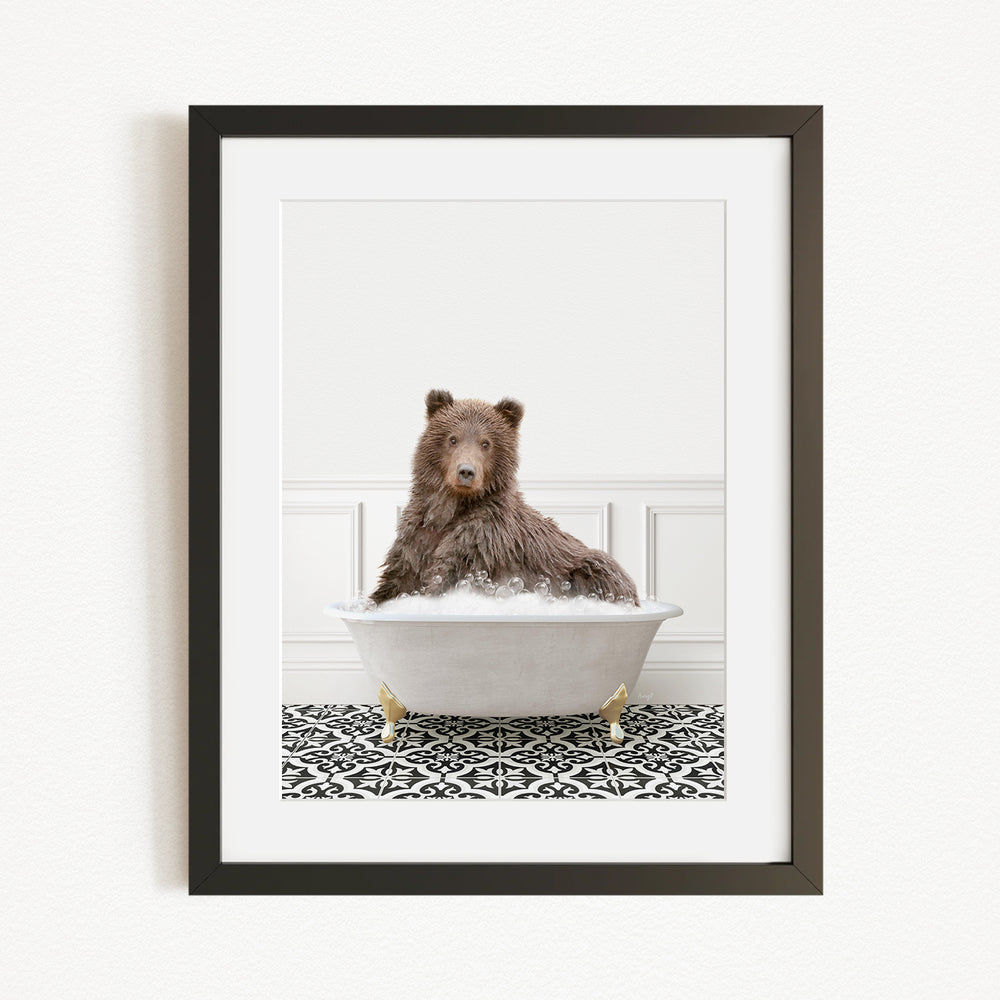 A brown bear sitting in a white bathtub filled with water, surrounded by a black and white patterned rug.
