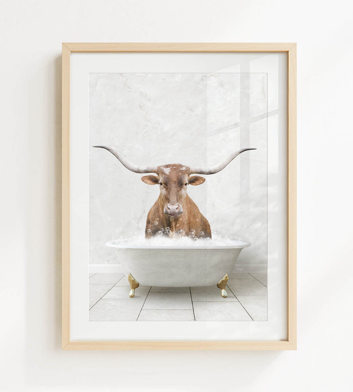 A framed image depicting a brown cow with long horns sitting in a white bathtub filled with water.