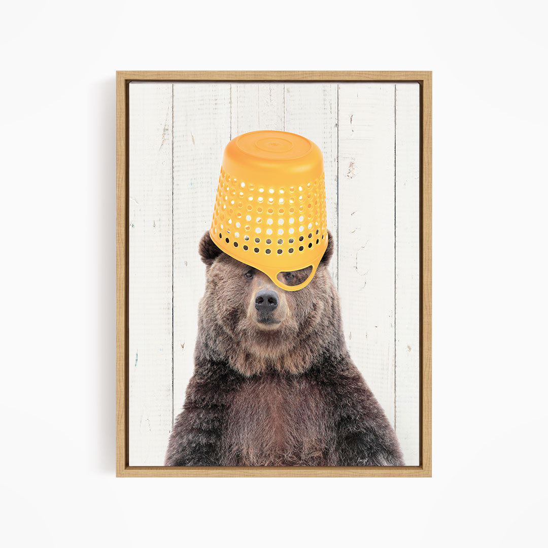 A brown bear wearing a yellow plastic bucket hat, with its eyes partially obscured by the hat.
