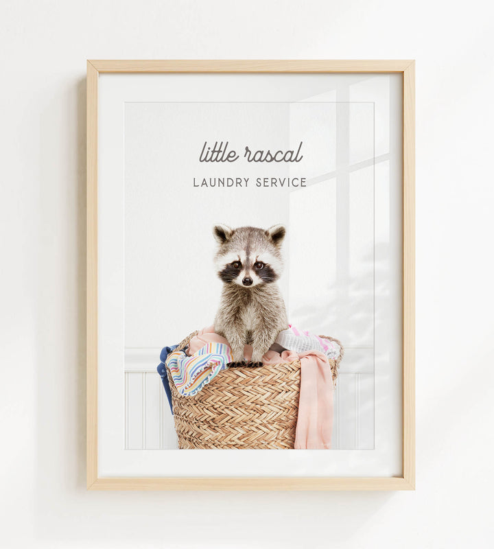 A raccoon sitting in a woven laundry basket, with the text "little rascal Laundry Service" displayed above it.