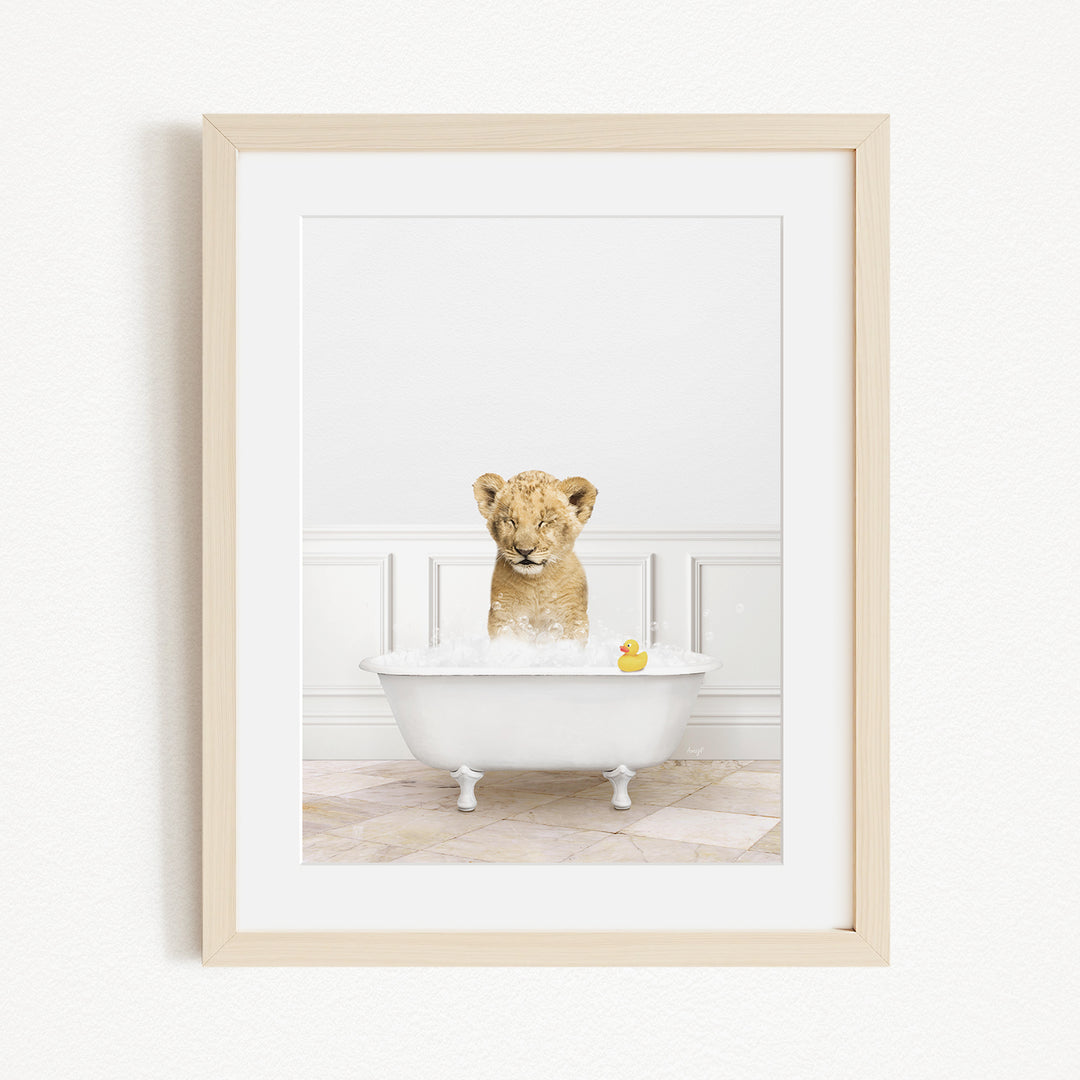 A young lion cub sitting in a white bathtub filled with water and bubbles, with a rubber duck floating in the water.