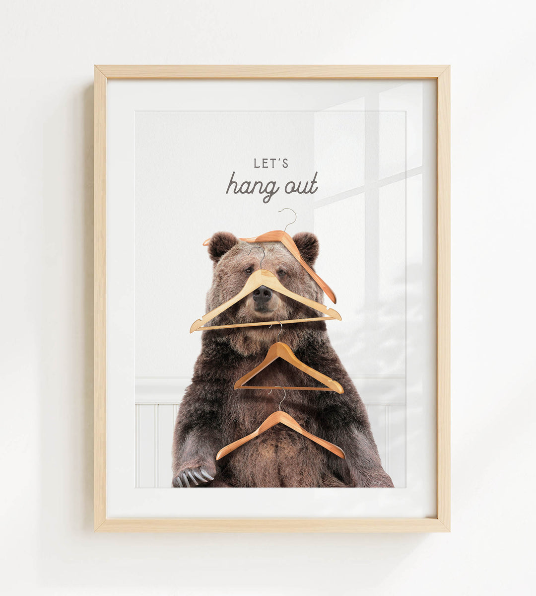 A framed image of a bear sitting on a shelf with multiple wooden hangers hanging from its head and neck, accompanied by the text "Let's hang out".