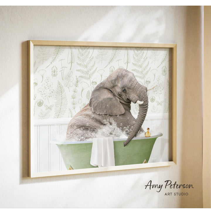 A framed photograph of an elephant sitting in a green bathtub filled with water, with a towel and a rubber duck nearby.