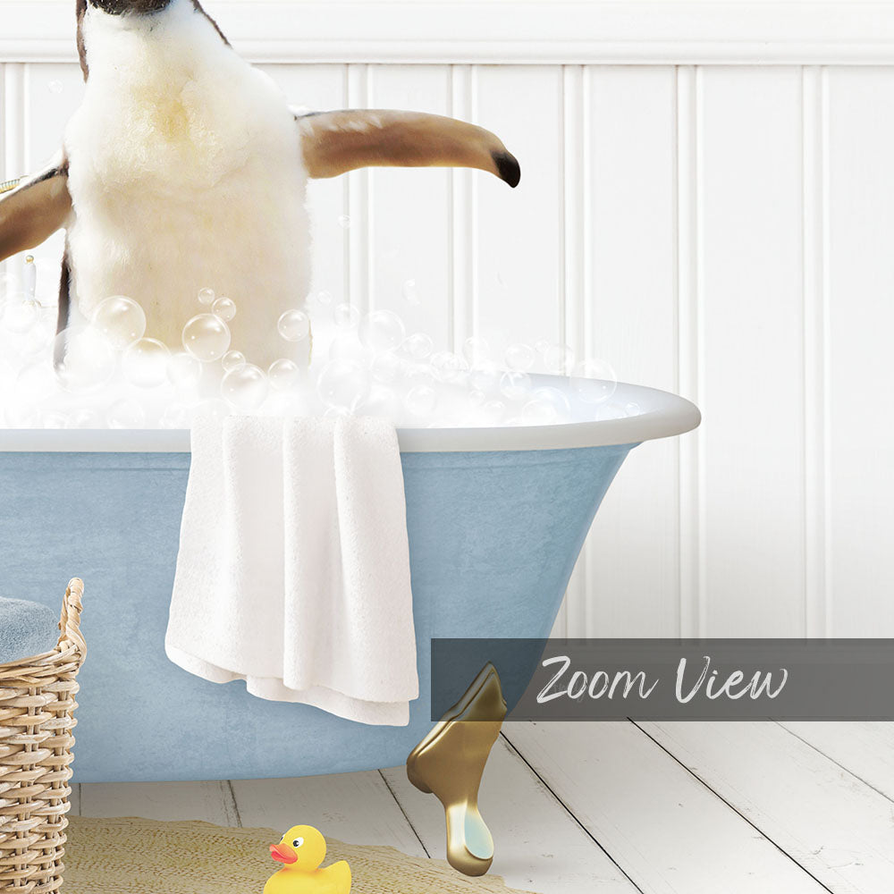 A penguin standing in a blue bathtub filled with bubbles, with a towel and rubber duck nearby.