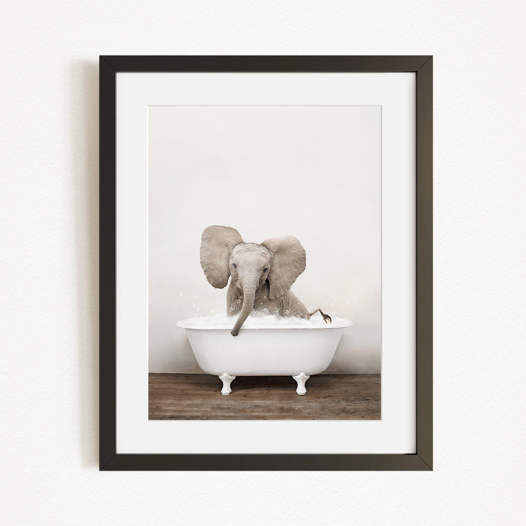 A baby elephant sitting in a white bathtub, surrounded by bubbles, with its trunk submerged in the water.