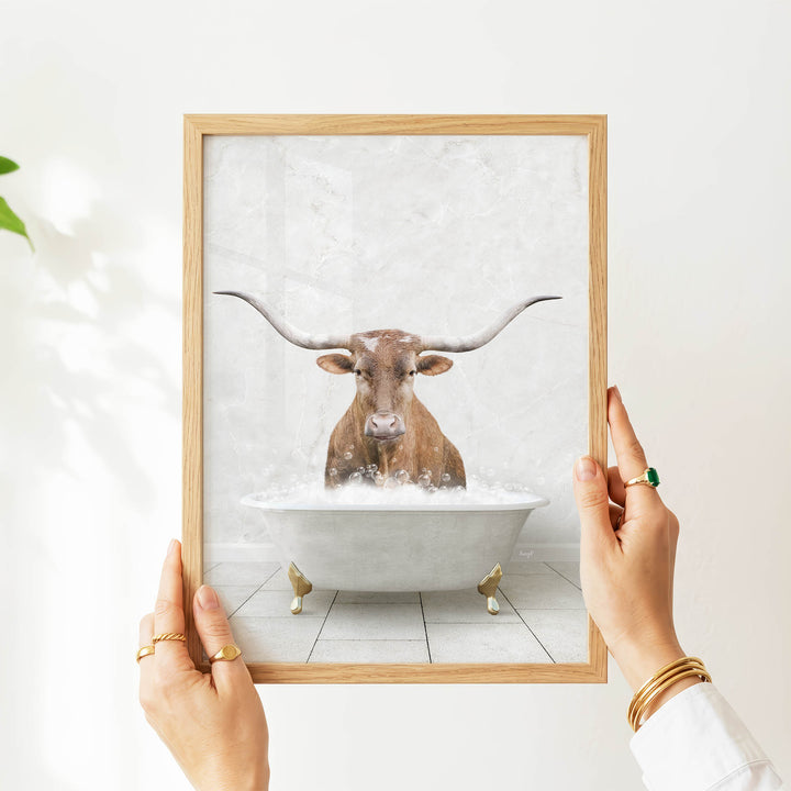 A person's hands are holding a framed picture of a bull with long horns, which is sitting in a bathtub filled with water.