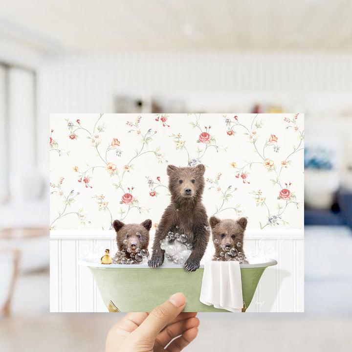 A hand holds up a collage of three images featuring a bear sitting in a bathtub with two other bears.