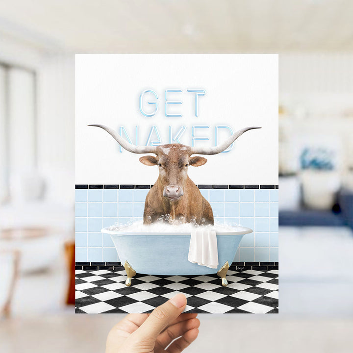 A hand holding a printed image of a bull with the text "GET NAKED" on a bathroom wall.