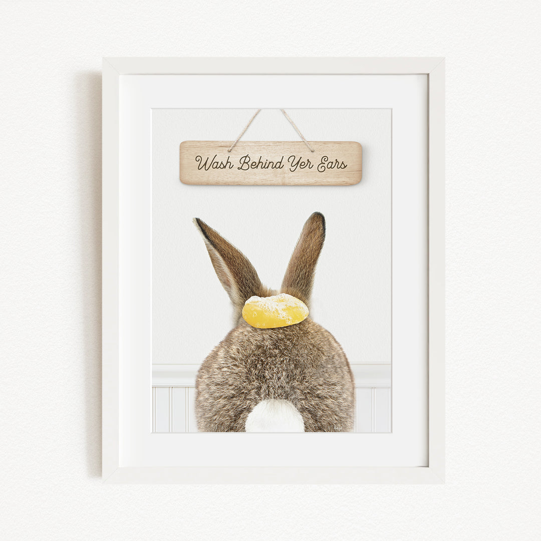 A framed image of a rabbit with a sign that says "Wash Behind Yer Ears" hanging above it.