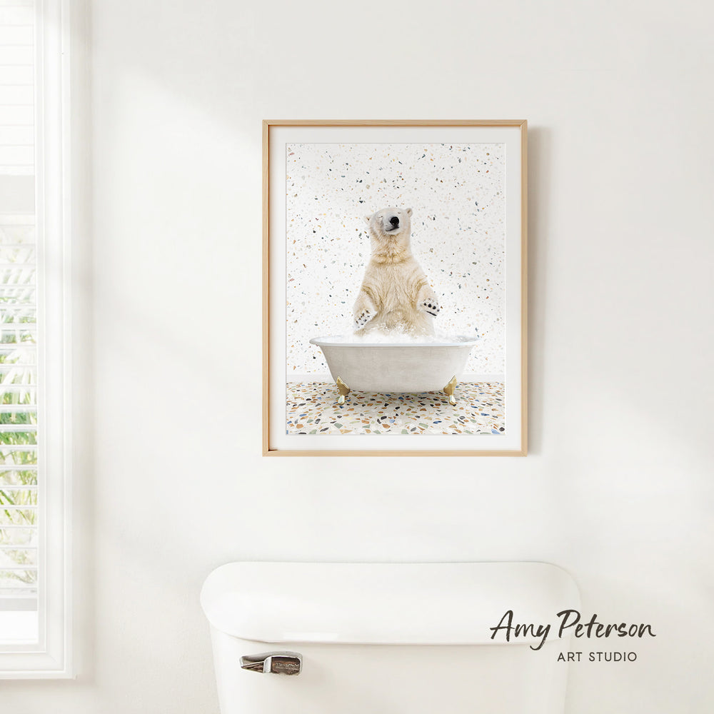 A framed print of a polar bear sitting in a bathtub is hanging on a white wall.