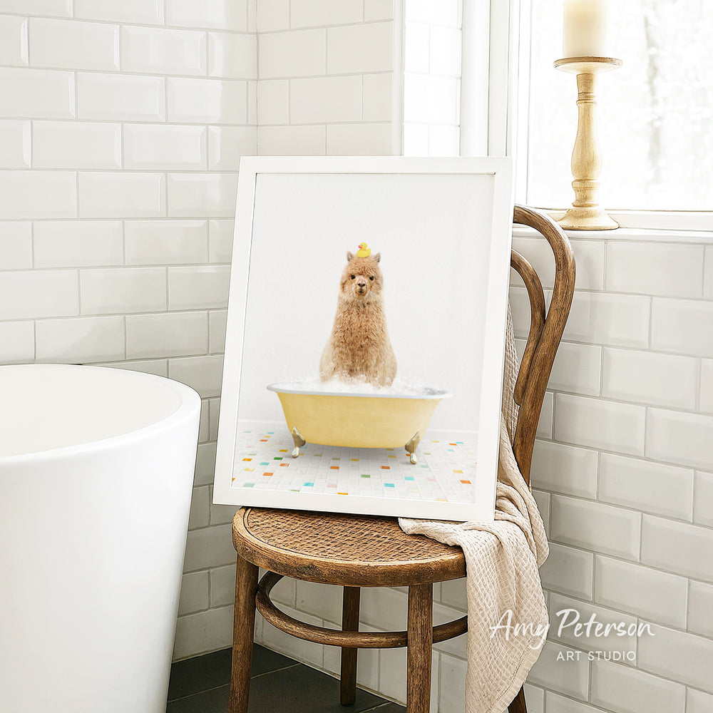 A framed image of a small dog sitting in a yellow bathtub filled with bubbles, with a towel draped over the back of a wooden chair in a bathroom setting.
