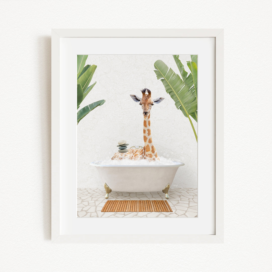 A giraffe sitting in a white bathtub filled with bubbles, surrounded by green leaves and a wooden mat on the floor.