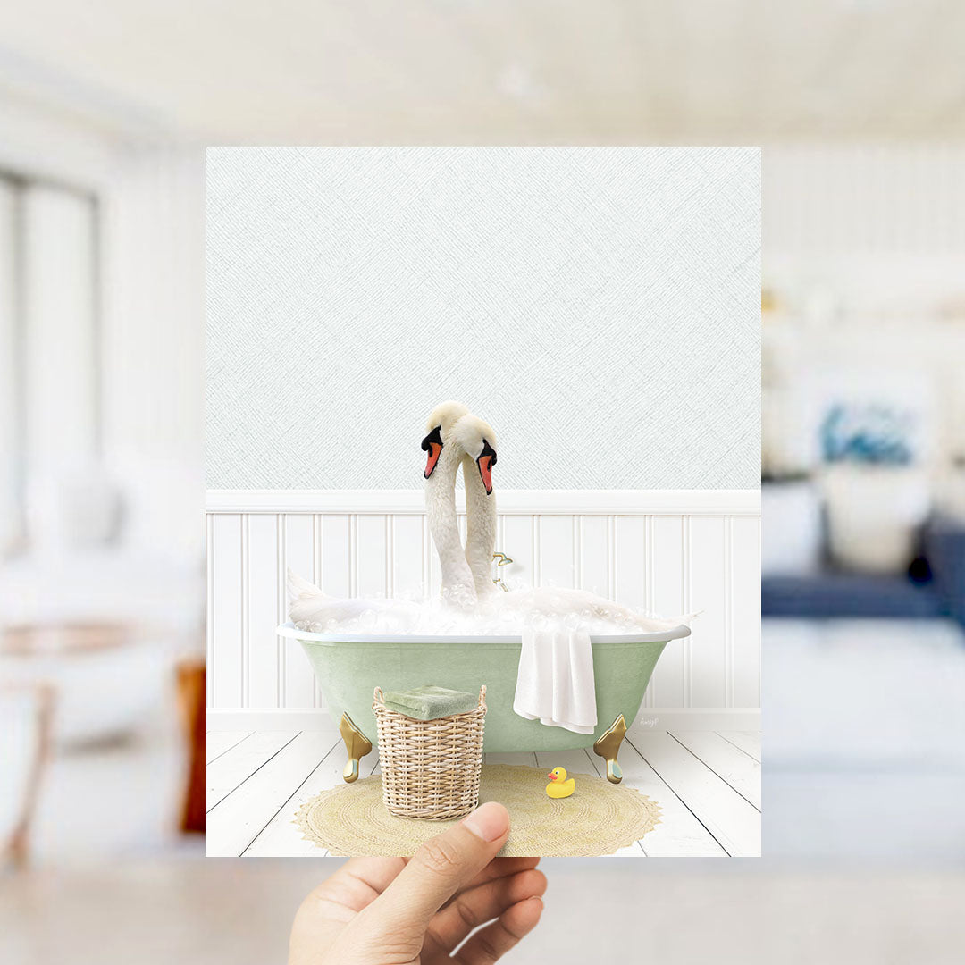 A hand holds up a framed image depicting two swans bathing in a green bathtub, with a basket of rubber ducks nearby.