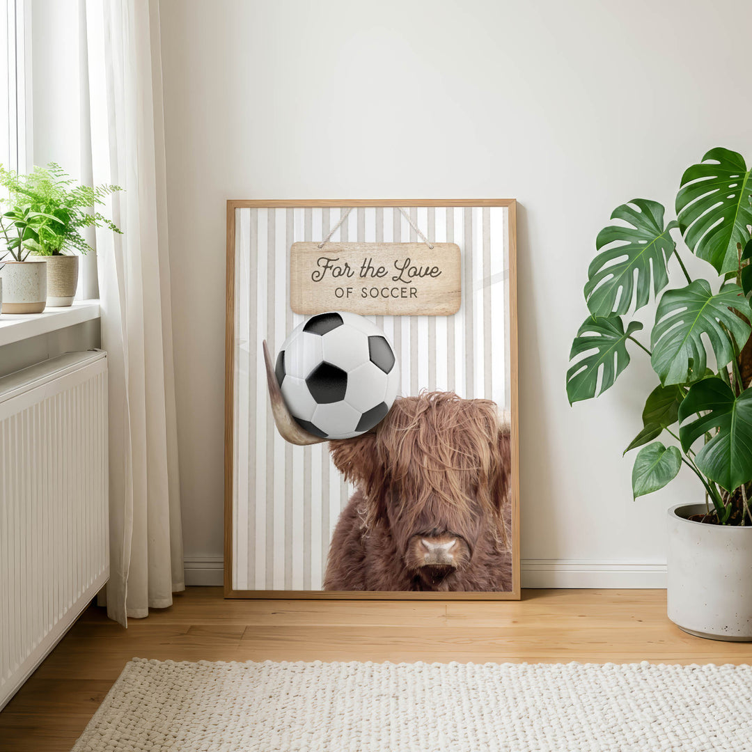 a framed poster with a close-up of a brown cow's head holding a soccer ball, along with a wooden sign that reads "For the Love of Soccer".