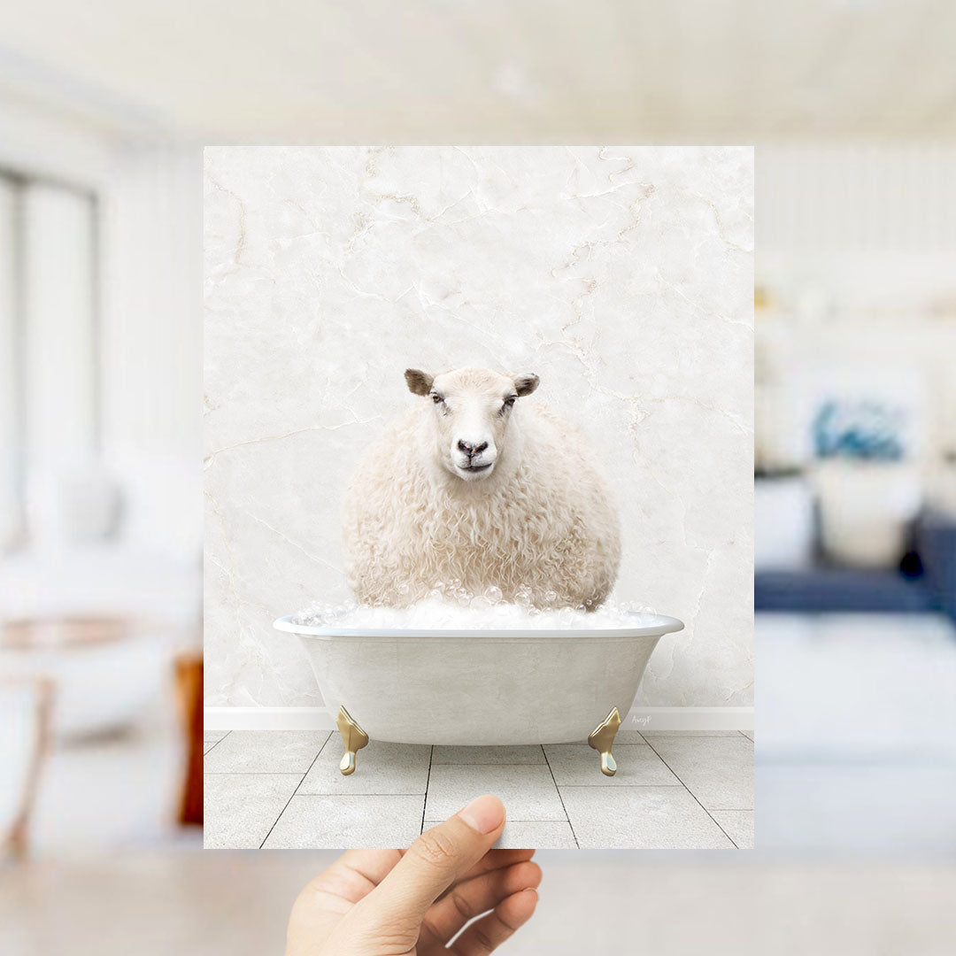 A fluffy white sheep sits in a white bathtub filled with bubbles, with a hand holding up the image to the camera.