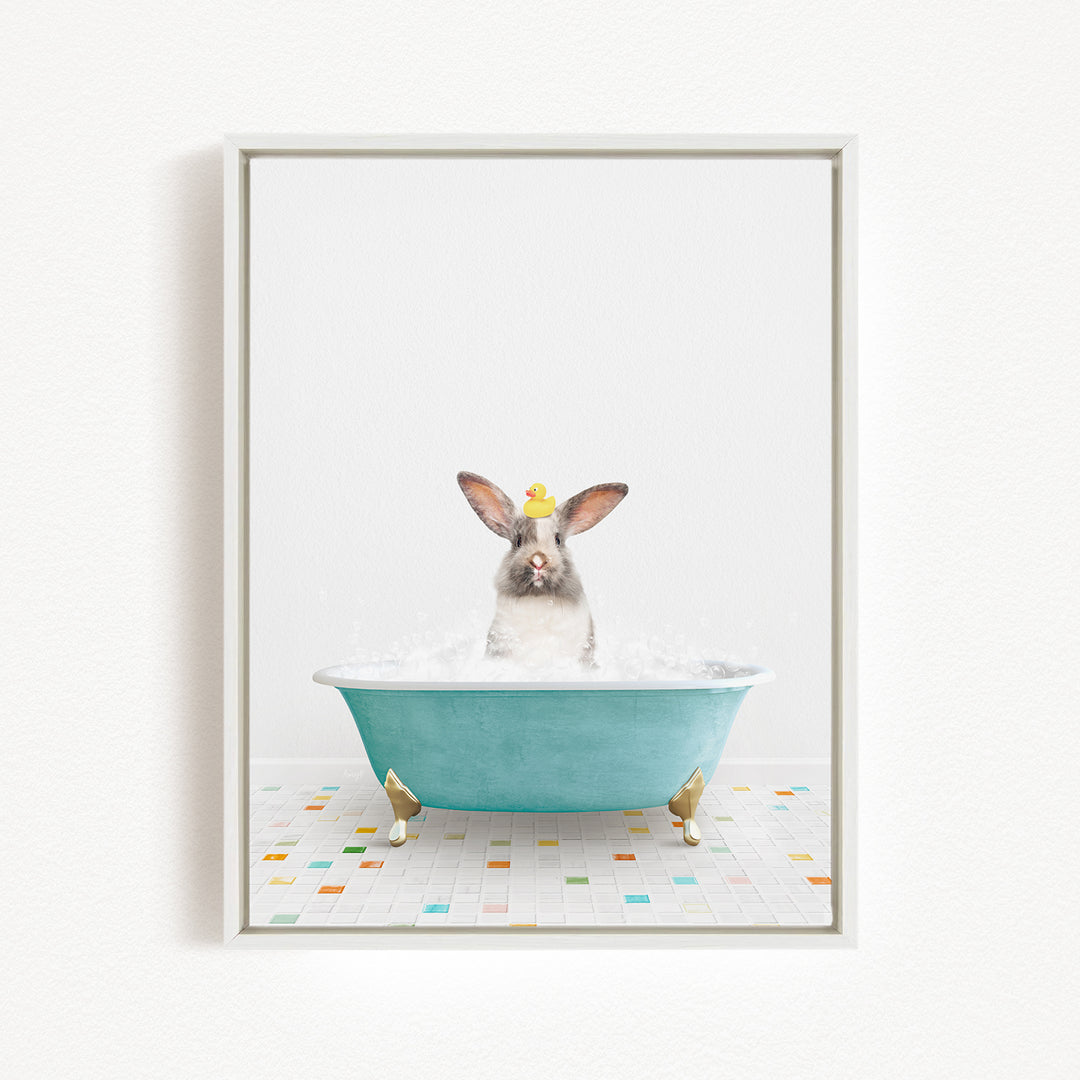 A gray and white rabbit sitting in a blue bathtub filled with bubbles, with a yellow duck perched on its head.