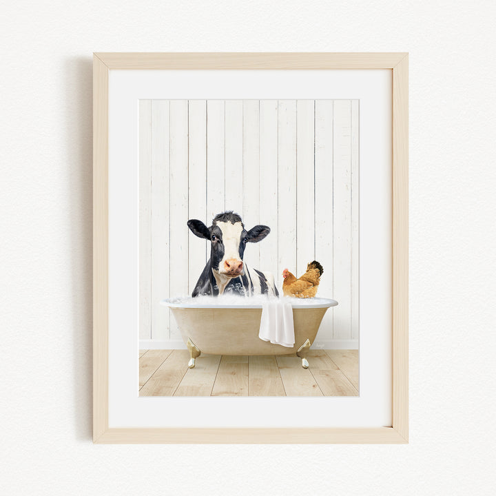 A black and white cow is sitting in a bathtub filled with water, with a chicken nearby, in a white wooden frame.