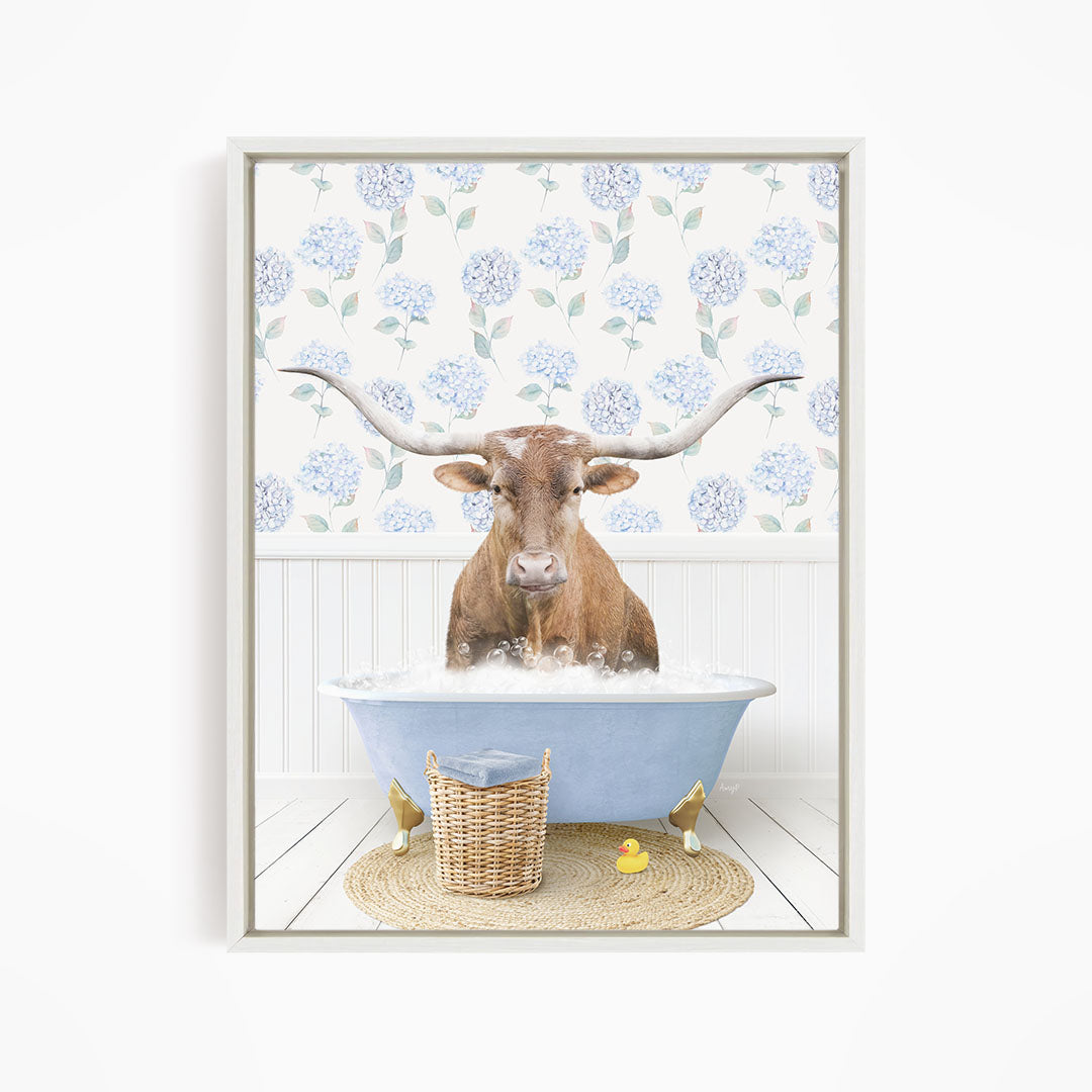 A brown cow with large horns is sitting in a blue bathtub filled with water, surrounded by a wicker basket and a yellow rubber duck.