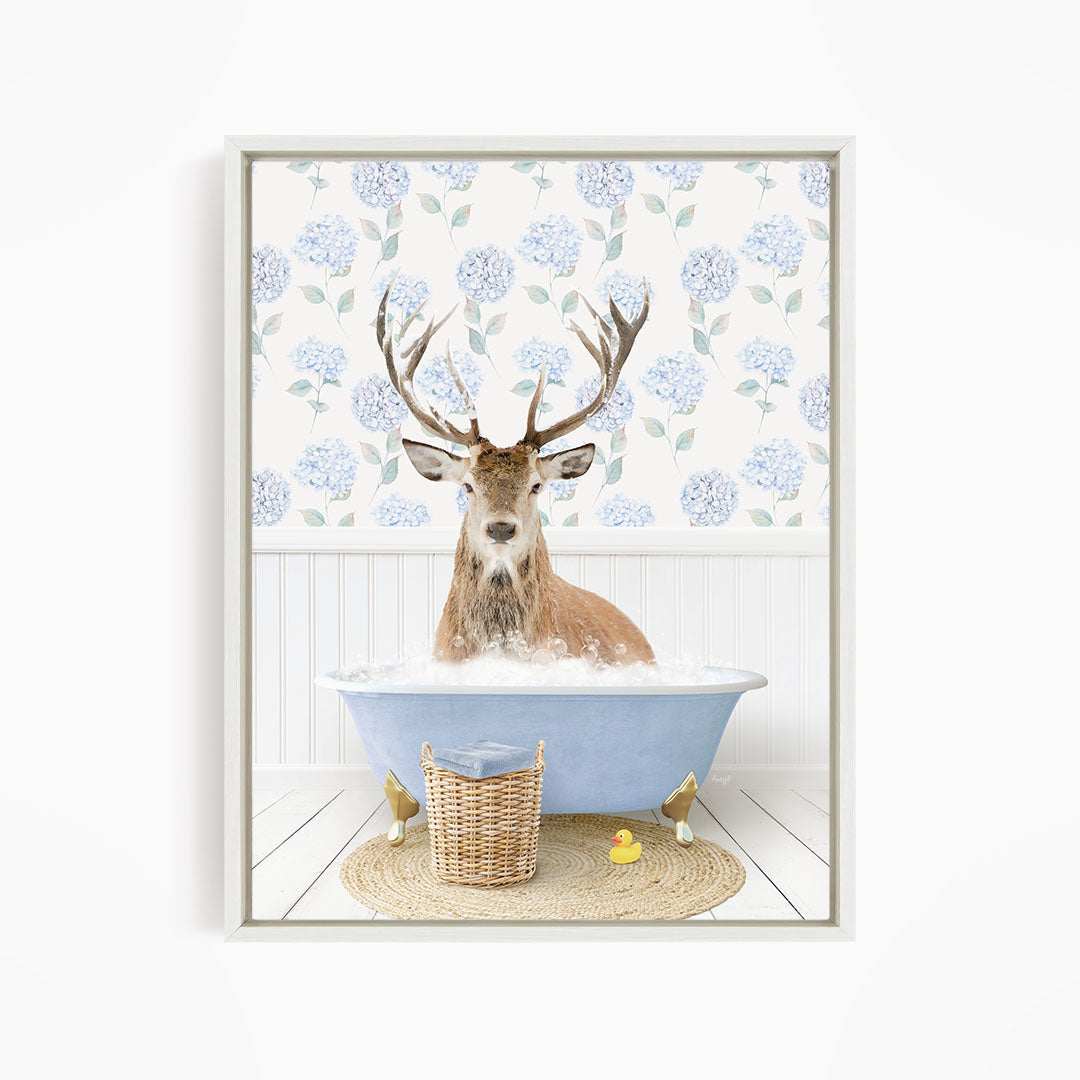 A deer with antlers is sitting in a bathtub filled with water, surrounded by a wicker basket and a yellow rubber duck.
