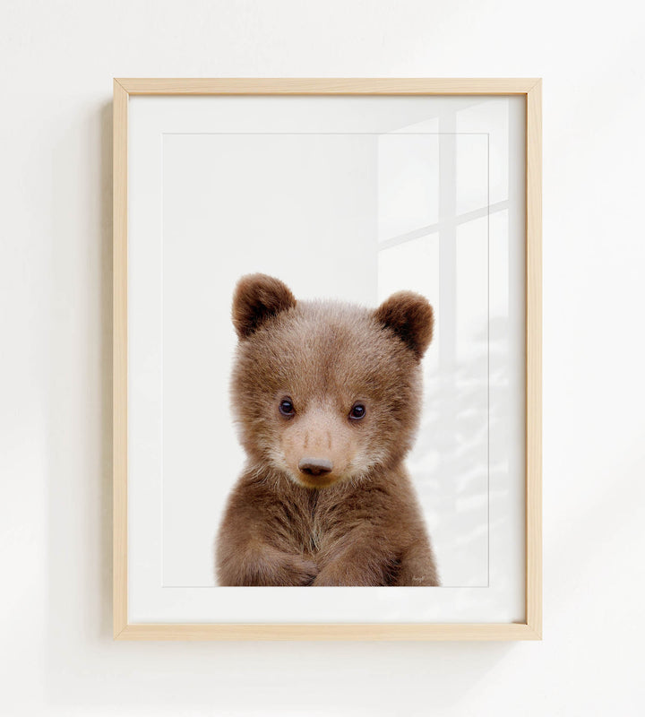 A cute brown bear cub with large eyes and a small nose is the focus of the framed image.