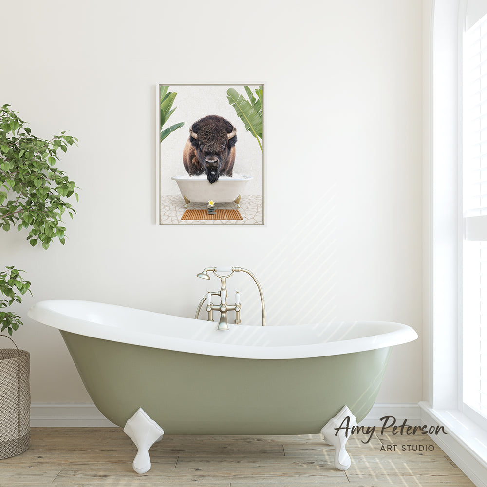 A framed image of a buffalo resting in a bathtub is displayed on the wall above a green clawfoot bathtub in a bathroom.