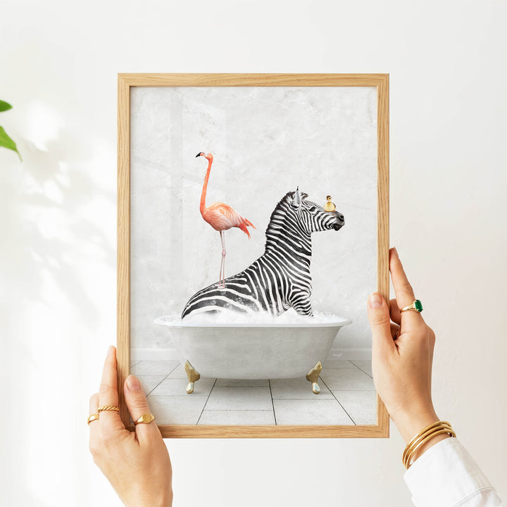 A person's hands are holding a framed picture of a zebra standing in a bathtub with a flamingo.