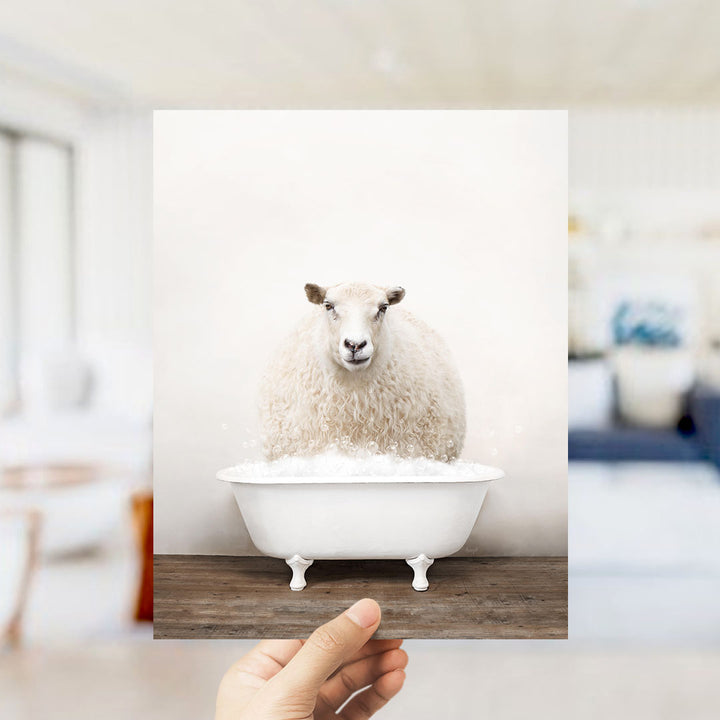 A fluffy white sheep sits in a white bathtub filled with bubbles, with a blurred background suggesting a bathroom setting.