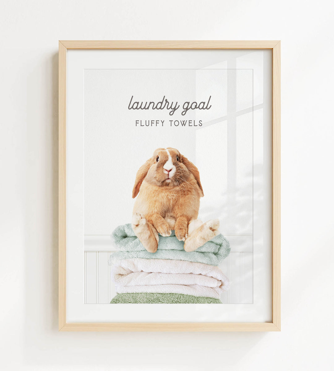A framed image of a rabbit sitting on a stack of fluffy towels, with the text "laundry goal" and "FLUFFY TOWELS" written above it.