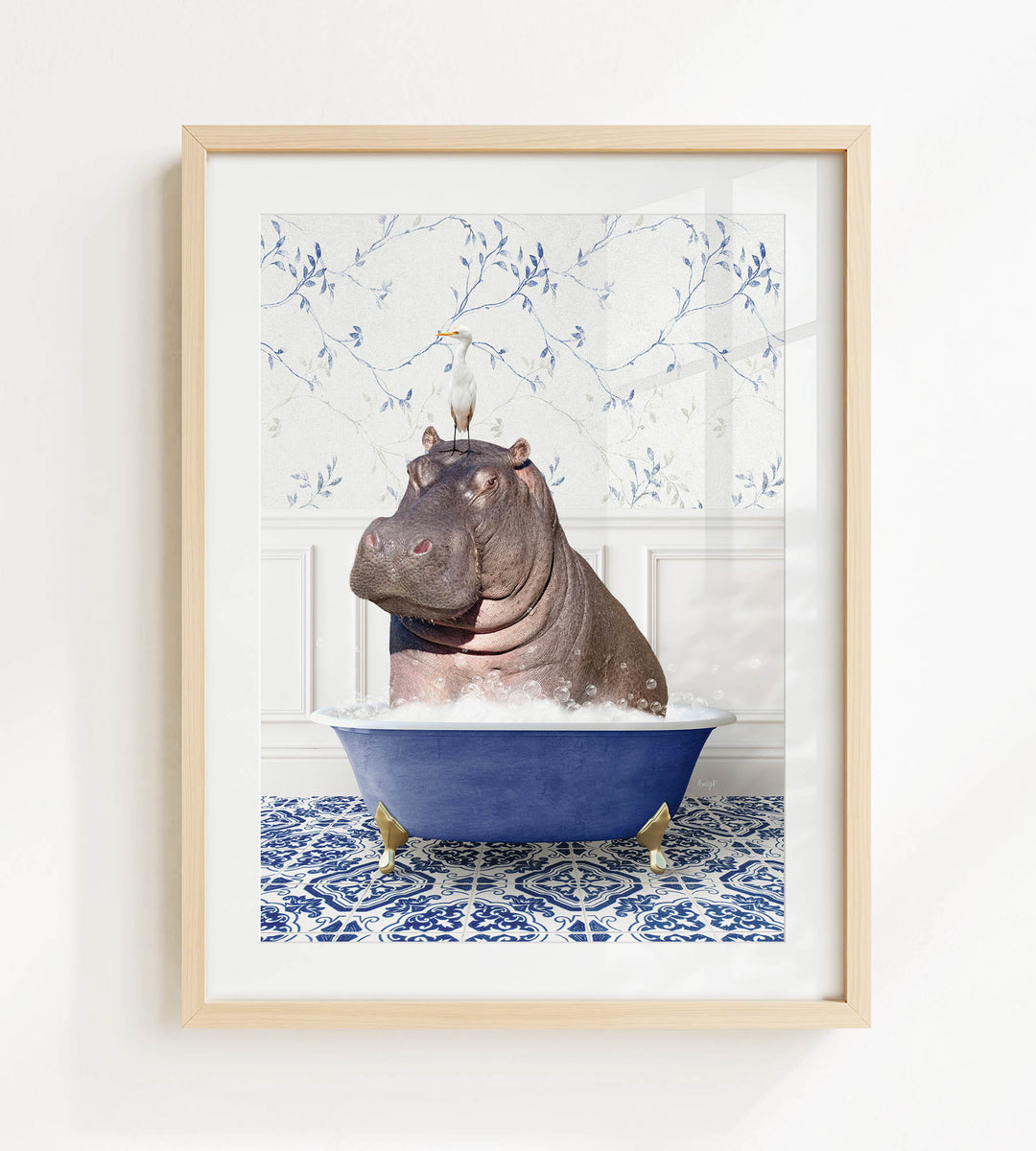A framed image depicting a hippopotamus sitting in a blue bathtub filled with water, surrounded by a blue and white patterned floor.