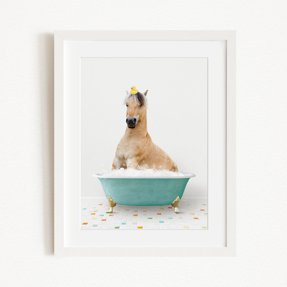 A light brown horse is sitting in a blue bathtub filled with bubbles, with a yellow rubber duck perched on its head.