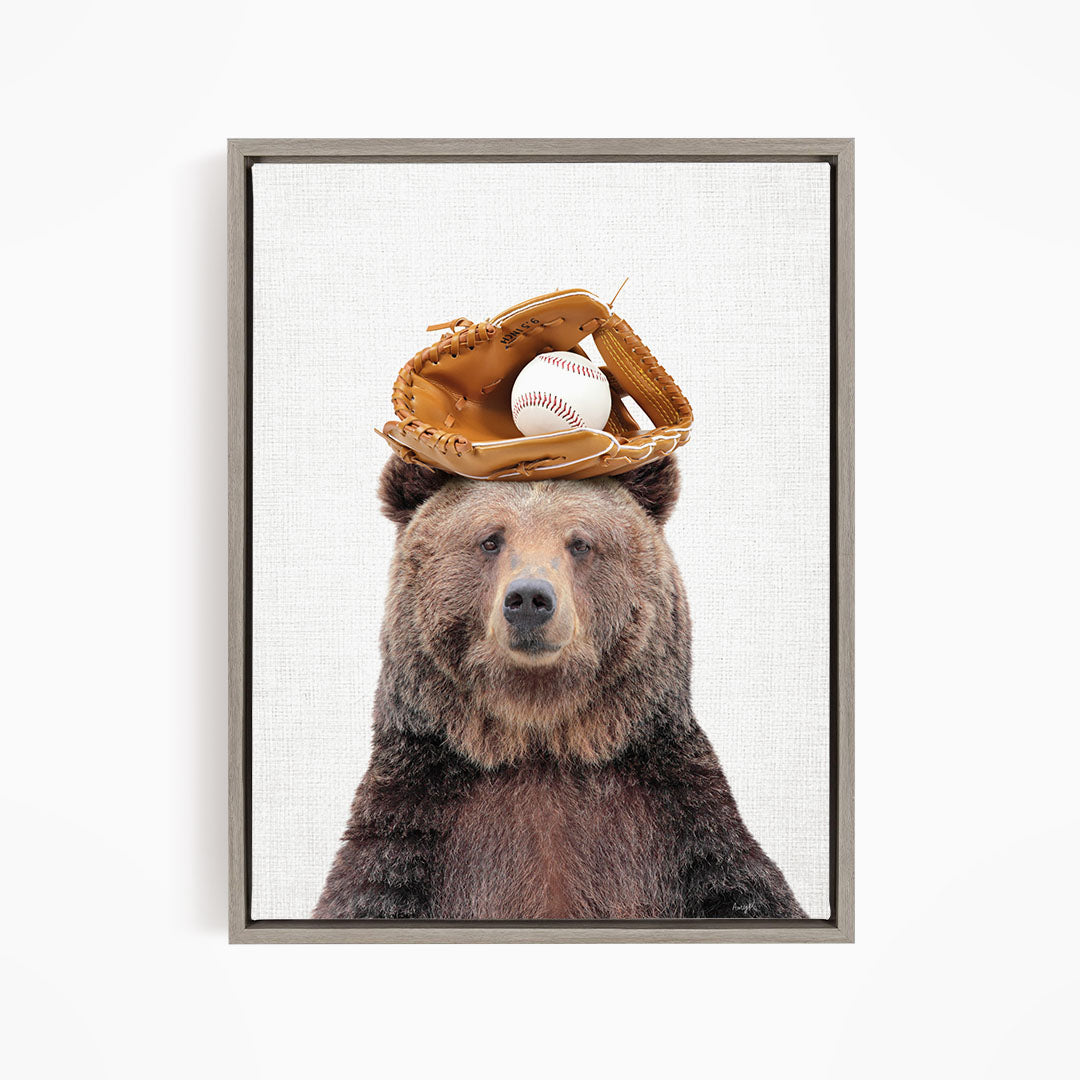 A brown bear wearing a baseball glove on its head, with a baseball resting on top of the glove.