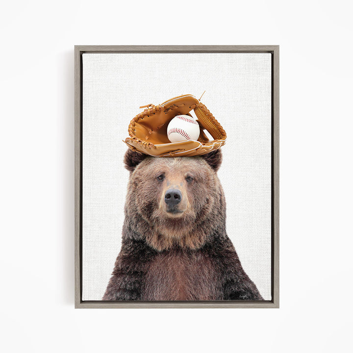 A brown bear wearing a baseball glove on its head, with a baseball resting on top of the glove.