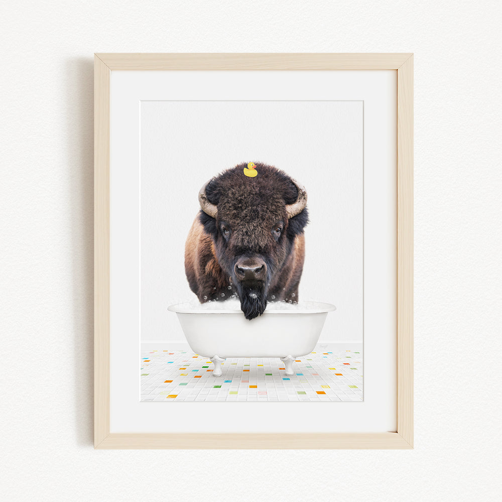 A buffalo with a yellow rubber duck perched on its head is standing in a white bathtub, surrounded by a colorful tiled floor.