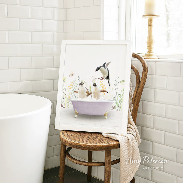 A framed illustration of two birds sitting in a bathtub, surrounded by flowers, is displayed on a wooden chair in a bathroom setting.
