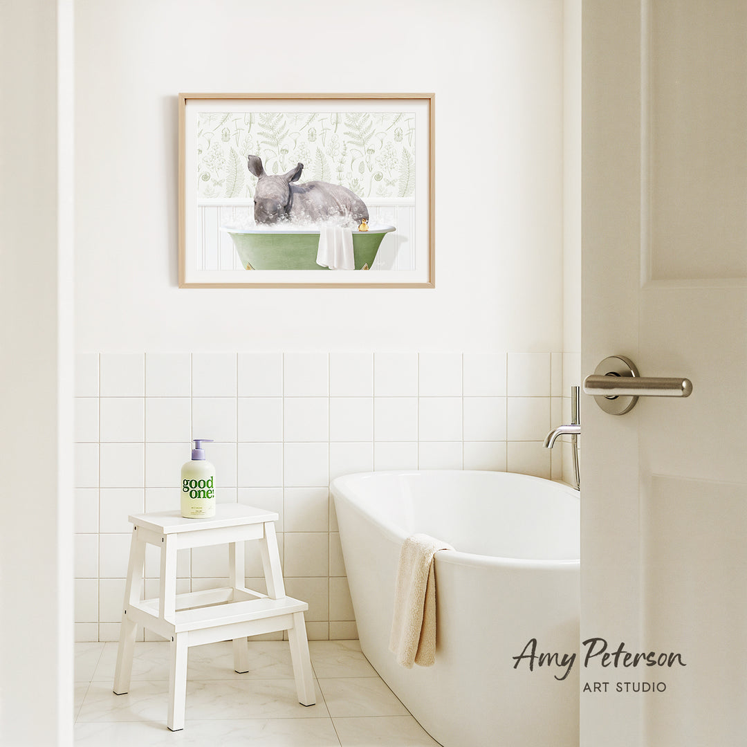 A framed painting of a rabbit sitting in a green bathtub is hanging on a white tiled wall above a white bathtub in a bathroom.