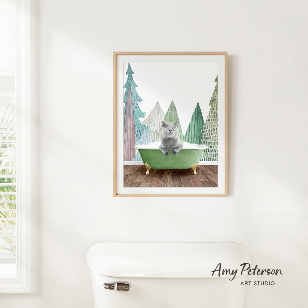 A framed print of a cat sitting in a green bathtub, surrounded by a snowy landscape with pine trees.
