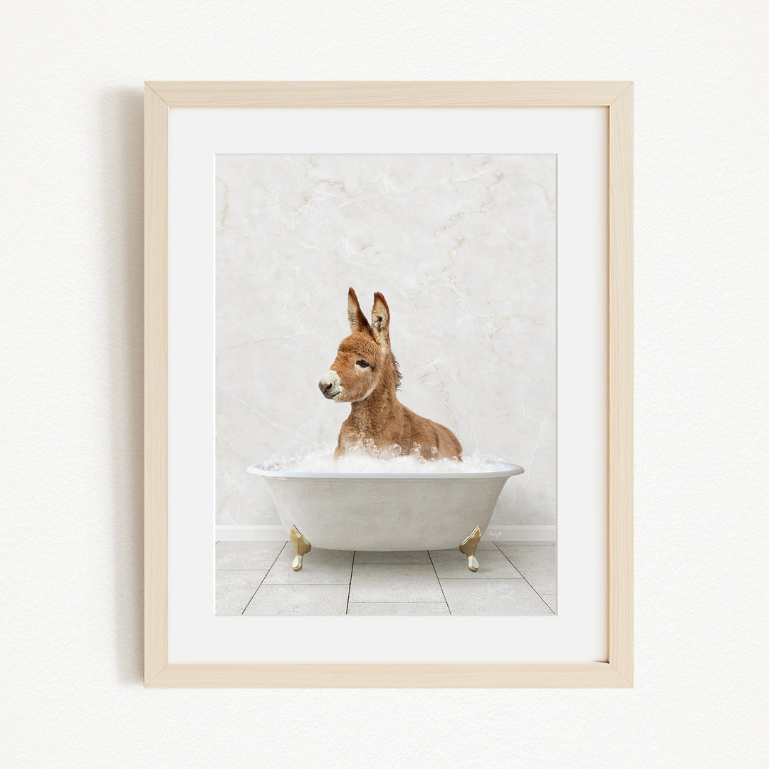 A donkey is sitting in a white bathtub filled with bubbles, looking directly at the camera.