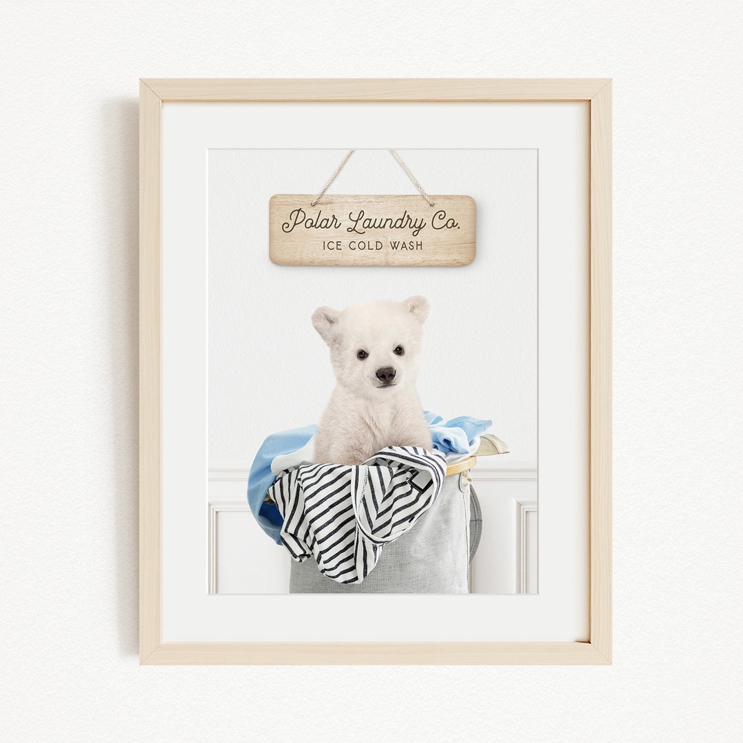A framed photograph of a white dog sitting in a laundry basket, with a wooden sign above it that reads "Polar Laundry Co. Ice Cold Wash".