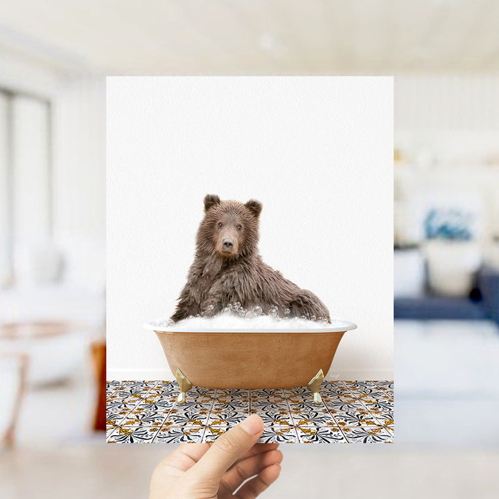 A brown bear sitting in a bathtub filled with bubbles, with a hand holding the image up to the camera.