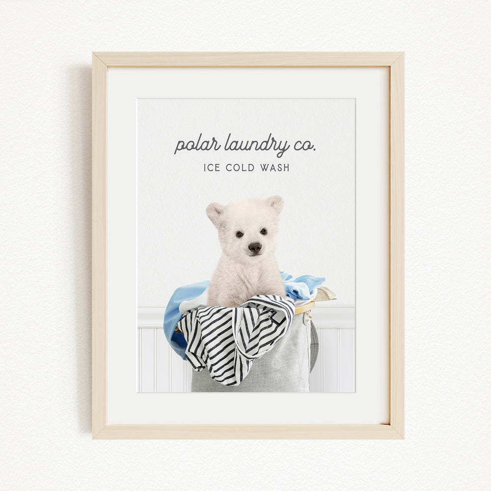 A framed image of a white dog sitting in a laundry basket filled with clothes, with the text "polar laundry co. ICE COLD WASH" displayed above the dog.
