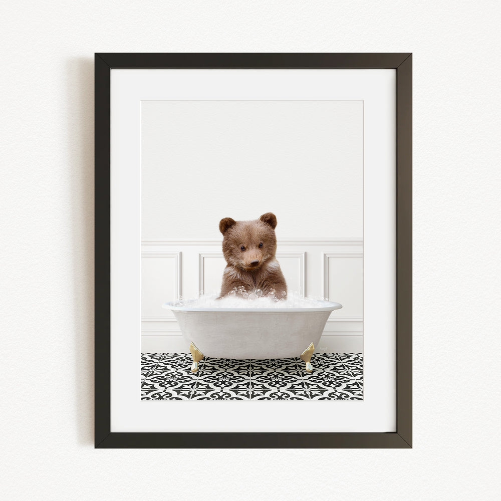 A cute brown bear sitting in a white bathtub filled with bubbles, surrounded by a black and white patterned rug.