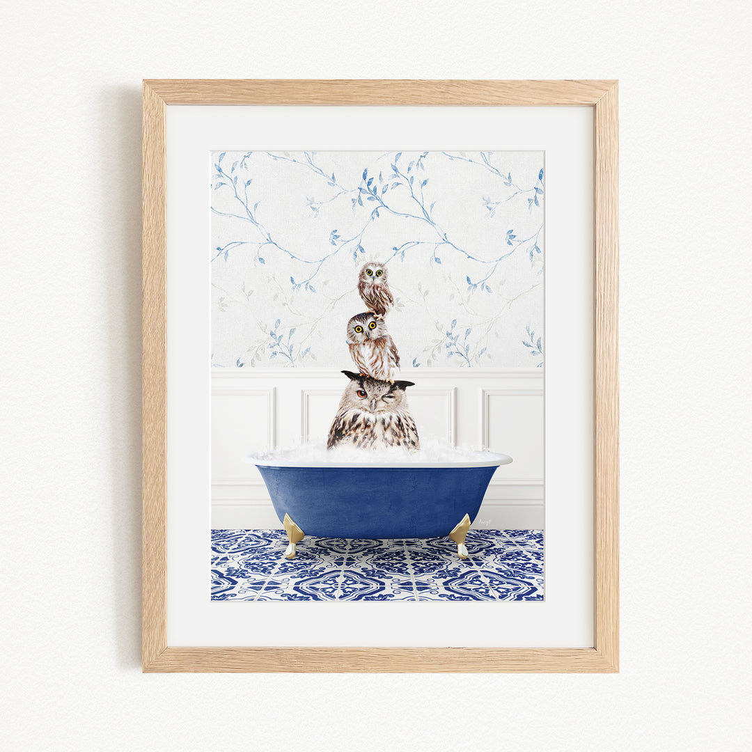 A framed image depicting a brown owl sitting in a blue bathtub filled with water, surrounded by a blue and white patterned tile floor.