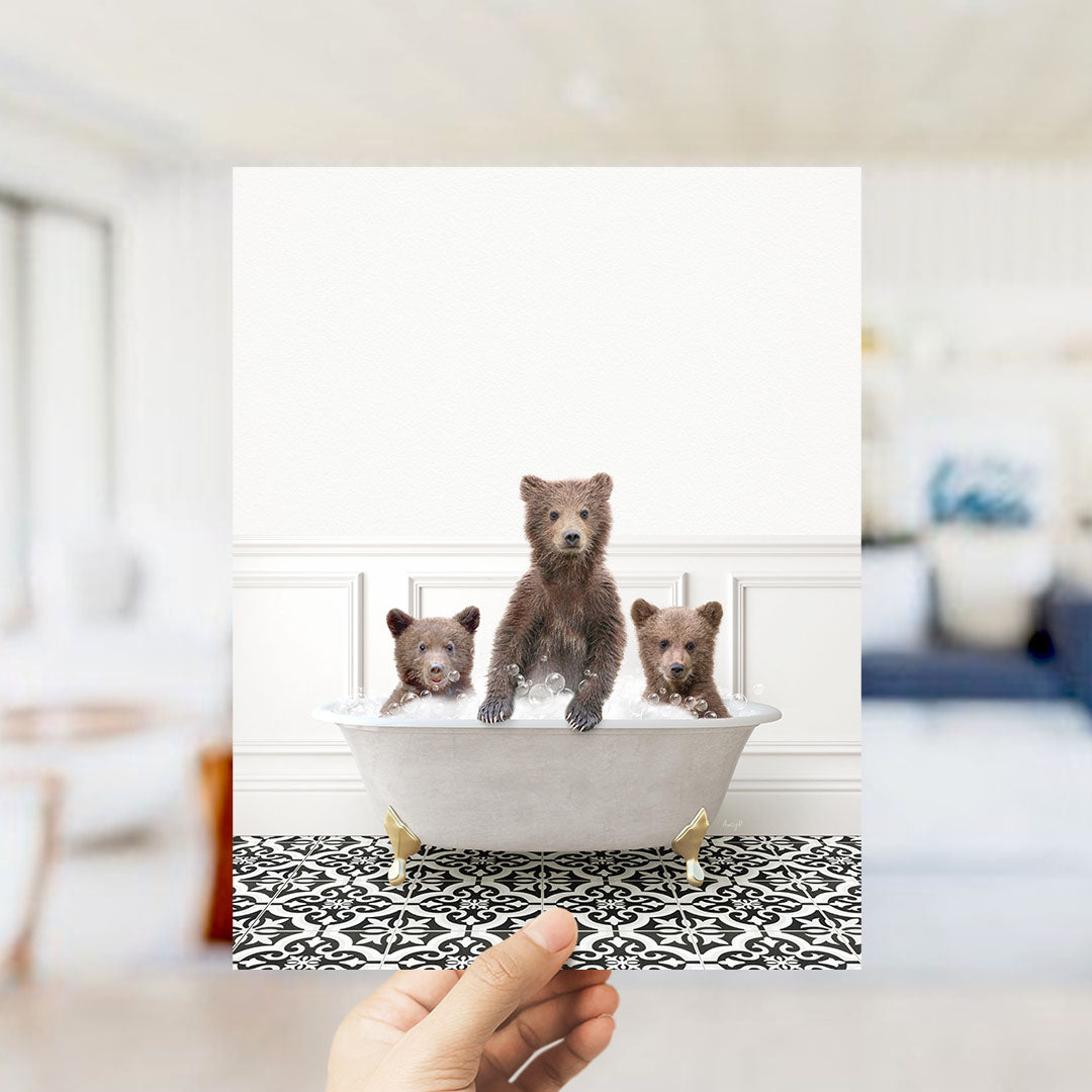 A hand holds up a framed image of three adorable brown bears sitting in a bathtub, with one bear sitting in the center and the other two on either side.