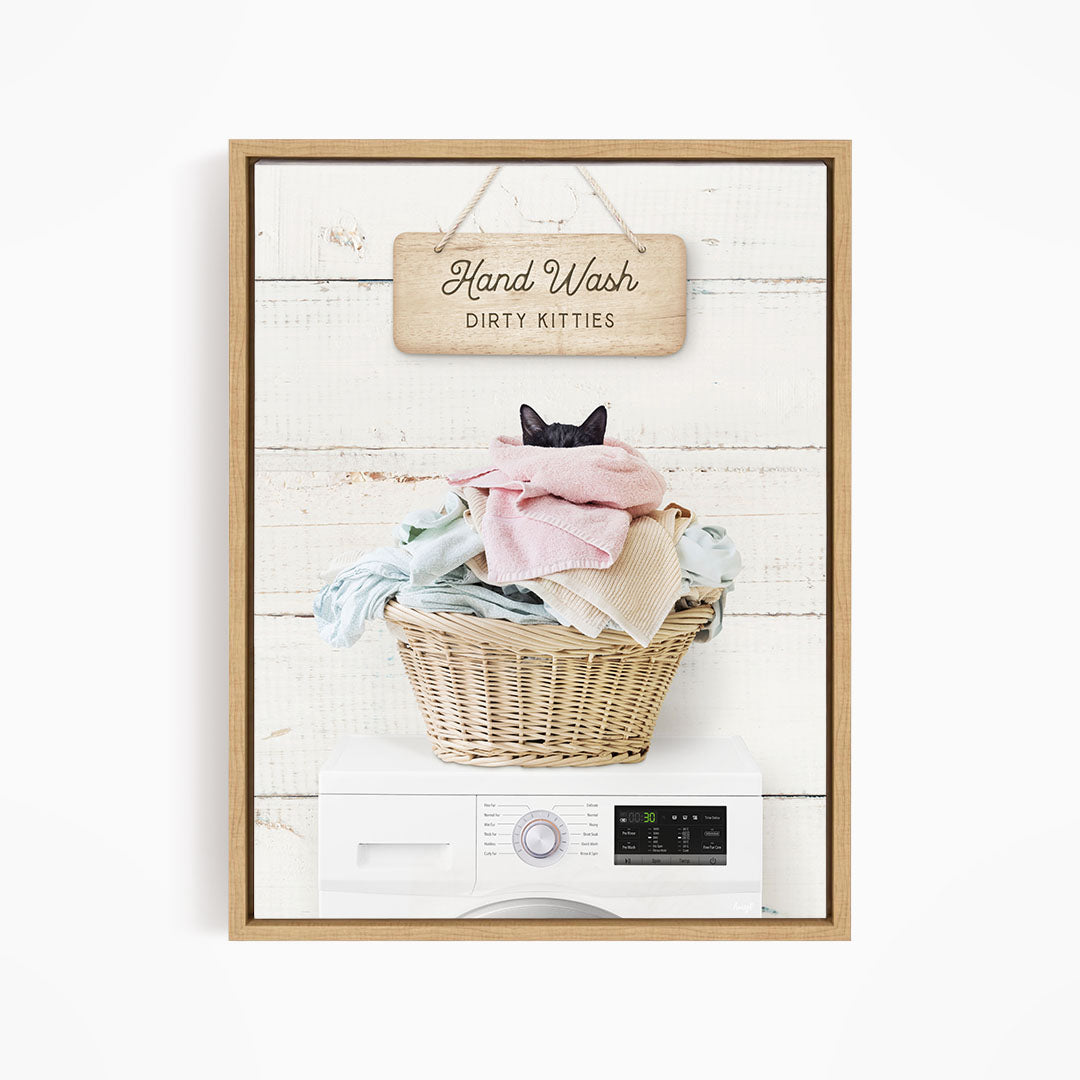 A framed image depicting a cat sitting in a basket filled with laundry, with a sign above that reads "Hand Wash Dirty Kittens".