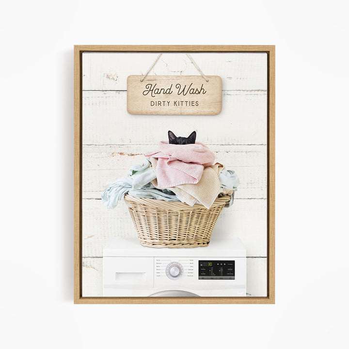 A framed image depicting a cat sitting in a basket filled with laundry, with a sign above that reads "Hand Wash Dirty Kittens".