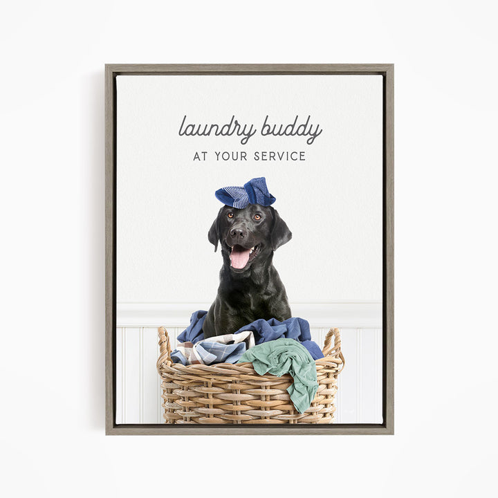 A black dog wearing a blue hat sits in a wicker laundry basket filled with clothes, with the text "laundry buddy at your service" displayed above the image.